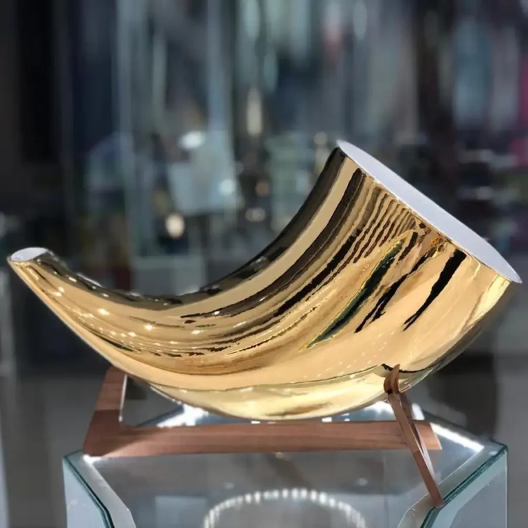 24K Gold Megaphone photographed on a glass display in a showroom, its polished gold horn reflecting the lights above a light wooden stand