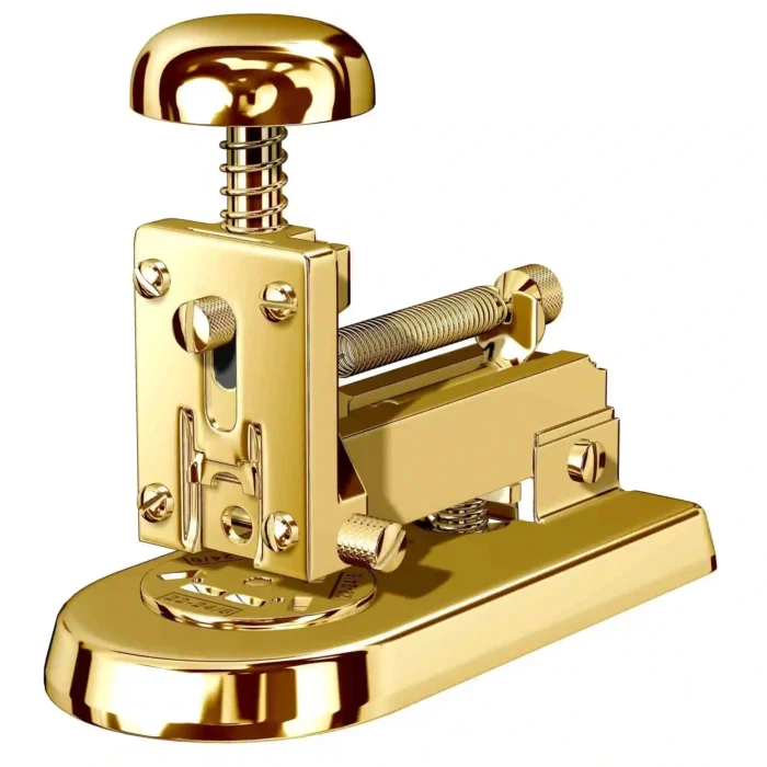 Gold Desk Stapler in three-quarter view, the domed 24K Gold knob riding on a coiled spring above a screwed faceplate, a spring-loaded magazine and a rounded base
