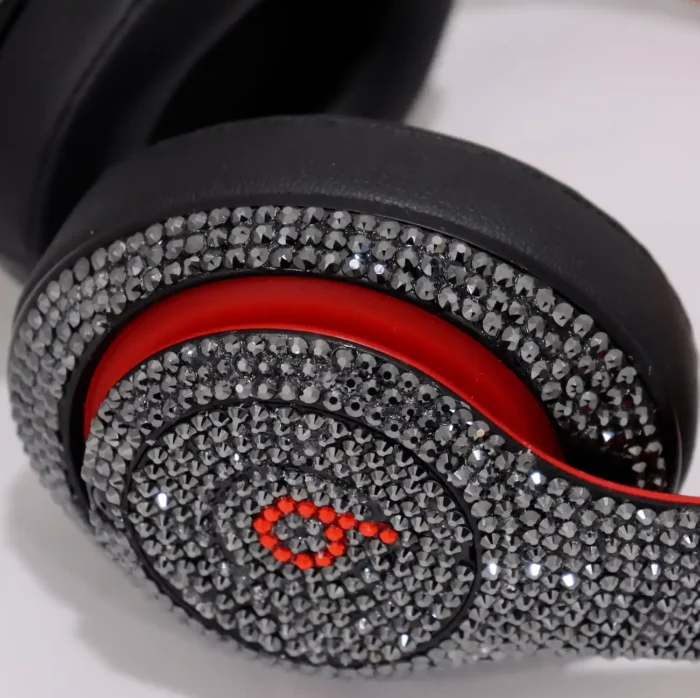 Swarovski Beats Studio Pro crystal work, shown on an earlier Beats Studio model: close-up of an outer ear cup in dark grey crystals, the b logo in red crystals beside that model’s red trim