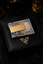 Gold Money Clip in 24K Gold holding folded US 100 dollar notes on a black leather box with the GoldPrivé emblem