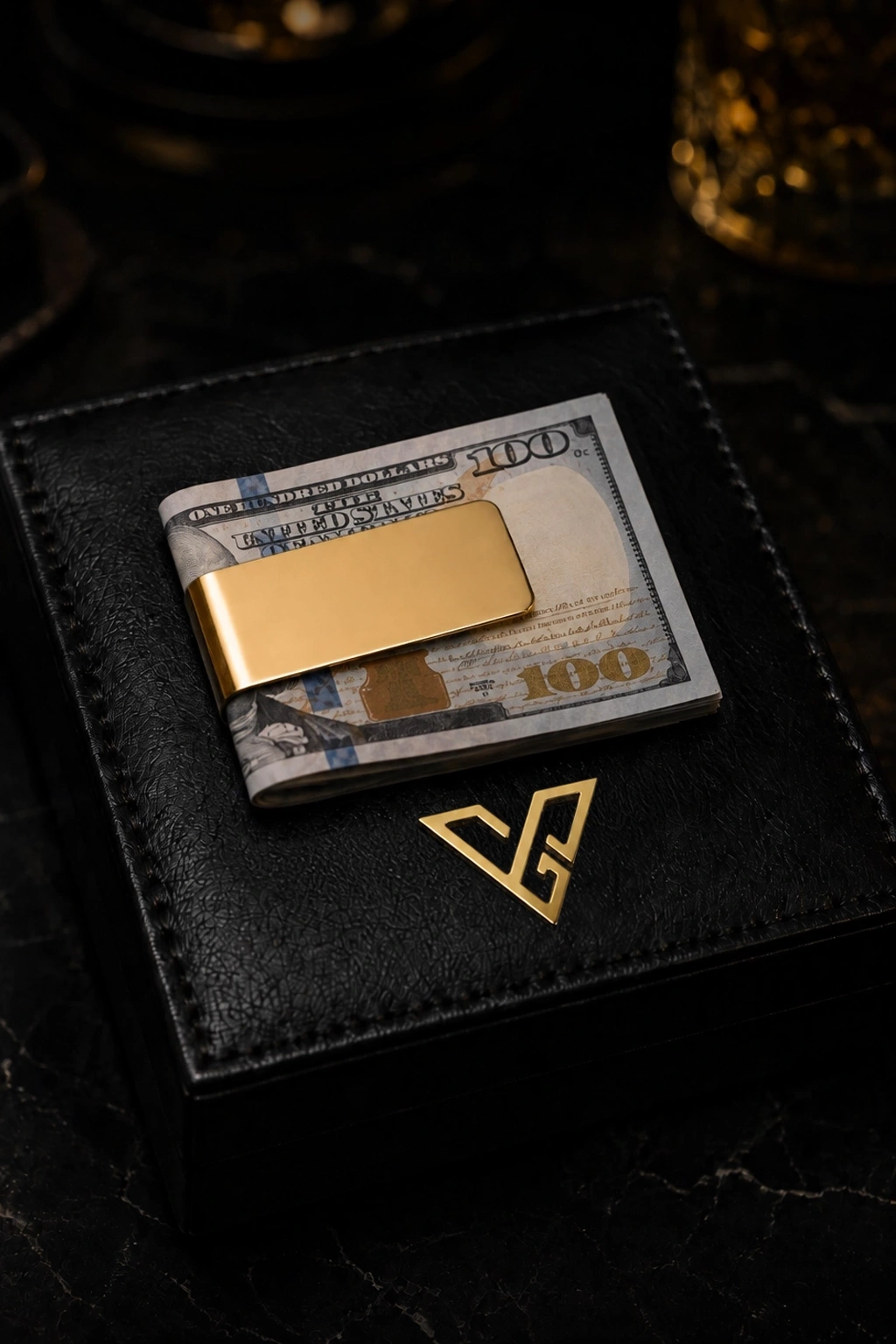 Gold Money Clip in 24K Gold holding folded US 100 dollar notes on a black leather box with the GoldPrivé emblem