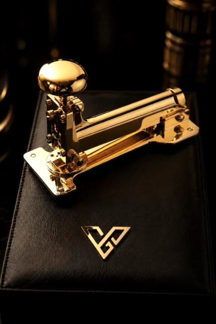 Gold Desk Stapler in 24K Gold on a black leather box, its mushroom plunger and long polished arm catching the light